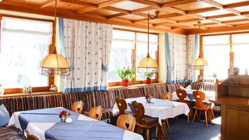 A cozy restaurant with wooden-paneled walls and large windows. The tables are decorated with blue tablecloths and the atmosphere feels inviting.