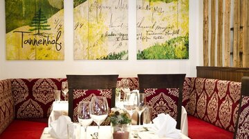 A cozy restaurant with elegantly set tables. Artistic paintings in soft colors hang on the wall.