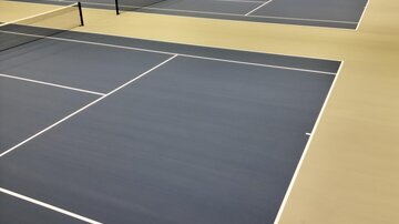 Eine moderne Tennishalle mit mehreren Spielfeldern. Die blauen Plätze sind gut beleuchtet und bereit für das Spiel.