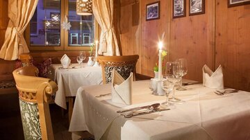 A cozy restaurant with wooden walls and soft lighting. The tables are elegantly set, creating an inviting atmosphere.