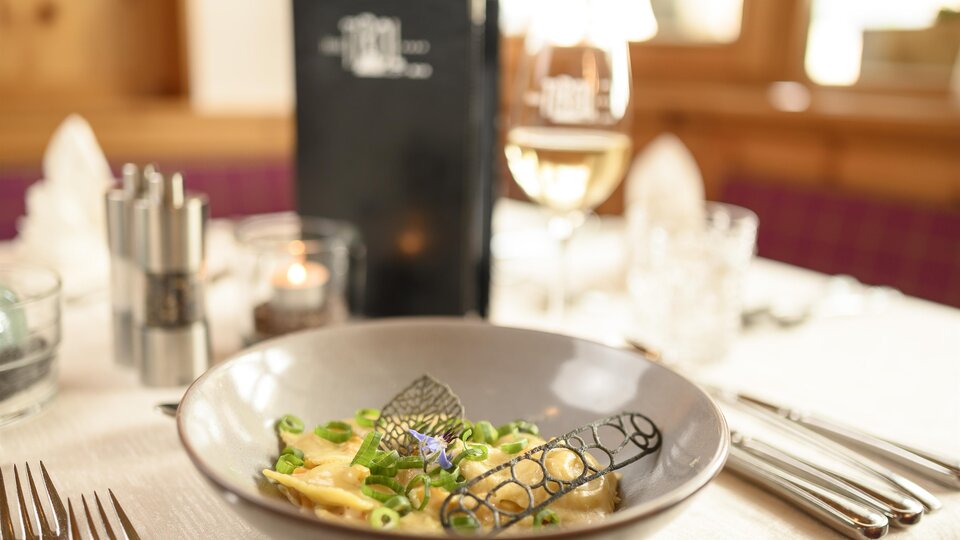 A stylishly set table with a plate of pasta and fresh vegetables. In the background, there is a drink and a menu card visible.