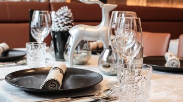 A festively set table with elegant glasses and silver decor. At the center is a stylish reindeer decoration piece.