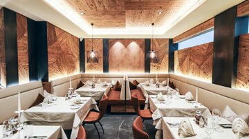An elegant restaurant with beautifully set tables and modern interior. The wooden ceiling and soft lighting create a pleasant atmosphere.