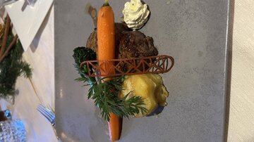An artfully arranged plate with meatballs, a carrot, broccoli, and a side of potatoes. On top, there is a small portion of cream.