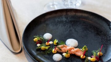 An elegantly arranged plate with shrimp and colorful vegetables. A glass of wine complements the upscale dish on the table.