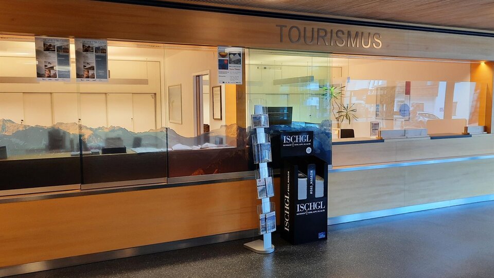 A reception area for tourism with a glass wall. On the floor, there is an information stand about the Ischgl region.