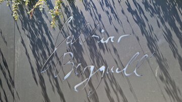 A black board with elegant writing. The name inscription is surrounded by shadows.