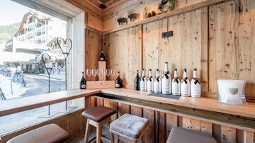 A cozy wooden bar with several bottles of wine on the table. A beautiful view outside is visible through the large window.