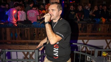 A man with a microphone stands in a club and sings. The crowd is visible in the background and is having fun.