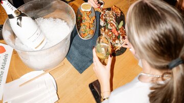 A lively celebration in a bar with many people. Two women are smiling at the table as they eat sushi and enjoy drinks.