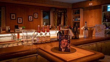 A cozy bar with wooden paneling and a selection of drinks. On the counter stands a bottle and a portrait of a man.