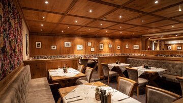 A cozy restaurant with wooden paneling and illuminated ceilings. The tables are neatly set, and there is a warm, inviting atmosphere.
