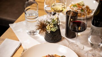 A beautifully set table with two plates of food, glasses of wine and water. In the foreground, there is a dish with rice and colorful vegetables.