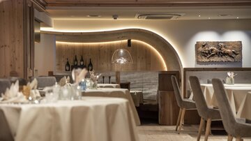 An elegant restaurant with wooden elements and soft lighting. Tables are tastefully set, and an artistic wall design gives the space character.