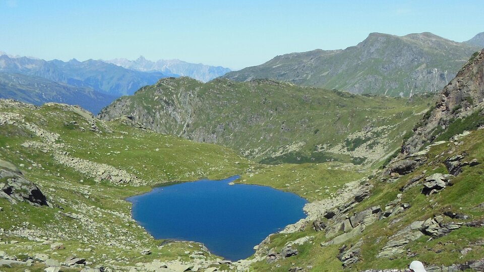 A beautiful mountain lake surrounded by green meadows and mountains. The sky is clear and blue.