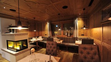 A cozy restaurant with wooden walls and a warm atmosphere. There are comfortable seating areas and a fireplace that enhances the ambiance.