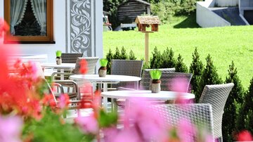 An inviting outdoor area with tables and chairs. Colorful flowers frame the scene and the green lawn provides a cheerful atmosphere.