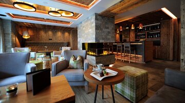 A modern café with cozy seating and rustic wooden decor. In the background, there is a bar with stylish lamps and a fireplace.