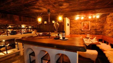 A cozy wine tavern with a wooden counter and soft lighting. The walls are made of stone, and soft furs on the seats create a warm atmosphere.
