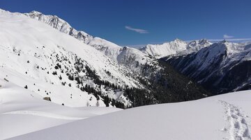 A snow-covered mountain landscape with a clear blue sky. The peaks rise majestically above the snow-covered valleys.