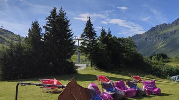 A beautiful outdoor area with sun loungers and a sign for the Bike Arena. The surrounding landscape is green and mountainous under a clear blue sky.