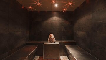 A relaxing wellness room with dark walls and a relaxation bench. In the center stands a salt stone on a pedestal.