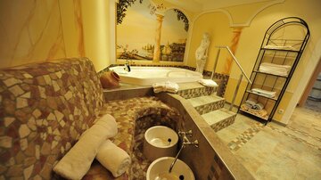 An elegant spa with a round hot tub and a cozy seating area. The walls are artistically painted and convey a relaxing atmosphere.