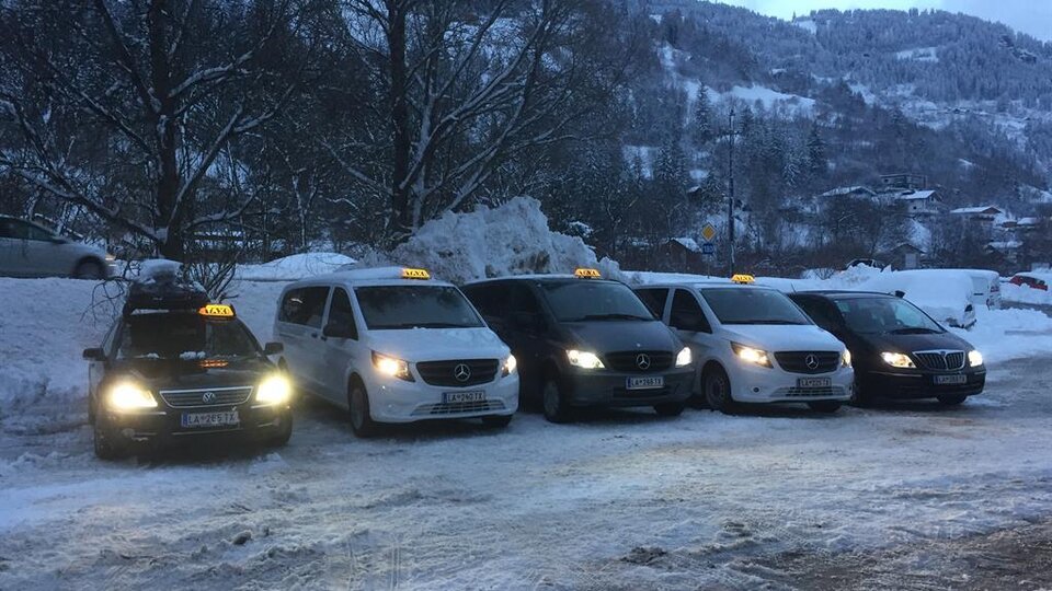 Five taxis are standing in a snowy environment. The vehicles are in different colors and are waiting for passengers.