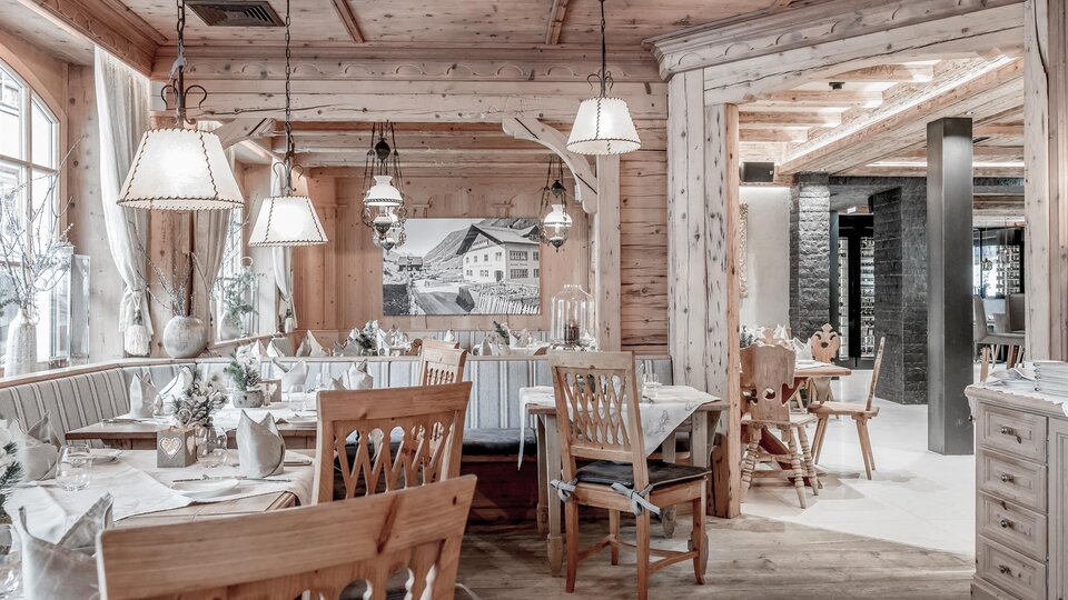 A cozy restaurant with wooden paneling and warm light. There are tables set with elegant tablecloths and wooden chairs.