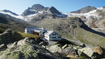 A beautiful mountain landscape with rugged rocks and tall peaks. In the foreground, there are two cabins nestled in nature.