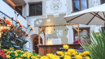 A beautiful courtyard with blooming flowers and an inn in the background. The wall is artistically designed and invites you to linger.
