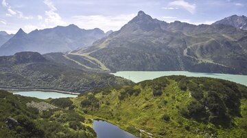 A breathtaking mountain landscape with green hills and a clear lake. In the background, majestic mountains rise up under a blue sky.