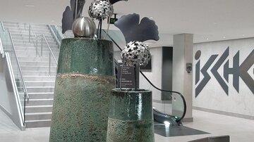 Two decorative ceramic vases, one larger and one smaller, are on a table. They are decorated with stylized flowers and modern accents.