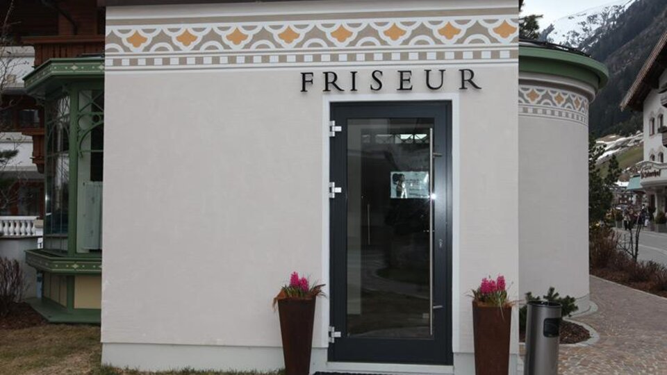 A hair salon with an elegant facade. The entrance door is modern and there are plants on both sides.