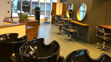 A modern hair salon with several wash basins and elegant hairdressing chairs. Large windows provide plenty of natural light.