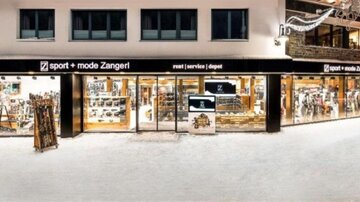 A sports and fashion store in a snowy area. The glass facade displays a variety of sports goods and apparel.