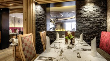 Ein elegantes Restaurant mit stilvollem Interieur aus Holz und Stein. Der Tisch ist schön gedeckt und es gibt eine gemütliche Atmosphäre.