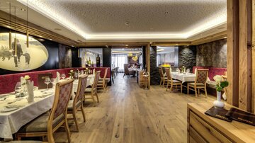 Ein gemütliches Restaurant mit Holzfußboden und eleganten Tischen. Die Wände sind geschmackvoll dekoriert und die Beleuchtung schafft eine einladende Atmosphäre.
