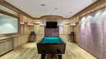 Ein stilvoller Spielraum mit einem Billardtisch in der Mitte. Im Hintergrund sind ein Fernseher und moderne Sitzmöglichkeiten zu sehen.