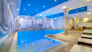 Ein moderner Innenpool mit hellem, blauem Wasser. Die Wände sind mit kunstvollen Murals und das Deckenlicht sorgt für eine angenehme Atmosphäre.