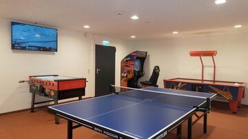 Ein Freizeitraum mit einem Tischtennistisch, einem Tischfußballspiel und einem Spielautomaten. Im Hintergrund ist ein Fernseher an der Wand.