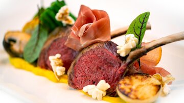 Ein kunstvoll angerichtetes Gericht mit Lammkoteletts, umgeben von frischen Kräutern und bunten Beilagen. Die Präsentation ist raffiniert und appetitlich.