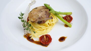 Ein elegantes Gericht mit Pasta, zartem Fleisch und frischem Gemüse. Die Präsentation wird durch getrocknete Tomaten und Kräuter ergänzt.