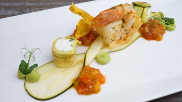 Ein elegant angerichtetes Gericht mit einer Garnelenportion und verschiedenen Gemüsesorten. Das Gericht wird durch Saucen und Garnituren dekoriert.