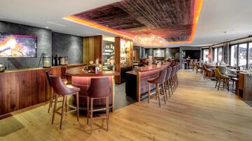 Eine moderne Bar mit Holzinterieur und gemütlichen Sitzgelegenheiten. Die Beleuchtung sorgt für eine einladende Atmosphäre.