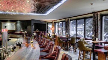 Eine elegante Bar mit einer langen Theke und bequemem Sitzbereich. Große Fenster bieten einen Ausblick auf die Umgebung.