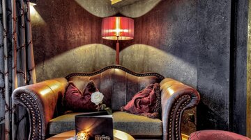 Ein gemütlicher Sitzbereich mit einem eleganten Ledersofa und dekorativen Kissen. Eine stilvolle Lampe und ein Tisch schaffen eine einladende Atmosphäre.