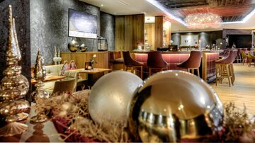 Eine moderne Bar mit eleganter Einrichtung und gemütlicher Atmosphäre. Goldene und silberne dekorative Elemente verleihen dem Raum einen festlichen Touch.