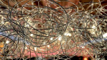 Ein wirres Netz aus Drahtschlingen mit warmem Licht im Hintergrund. Die Struktur erzeugt ein interessantes und modernes Ambiente.