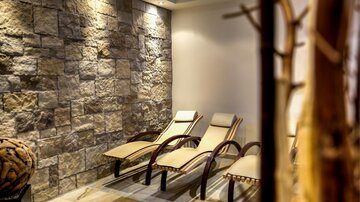 Ein entspannender Raum mit Liegen und einer Steinwand. Die Beleuchtung schafft eine ruhige Atmosphäre.